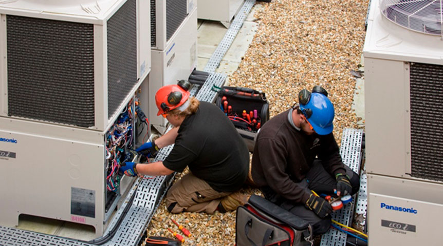 An image of two workers installing Panasonic VRF systems outside